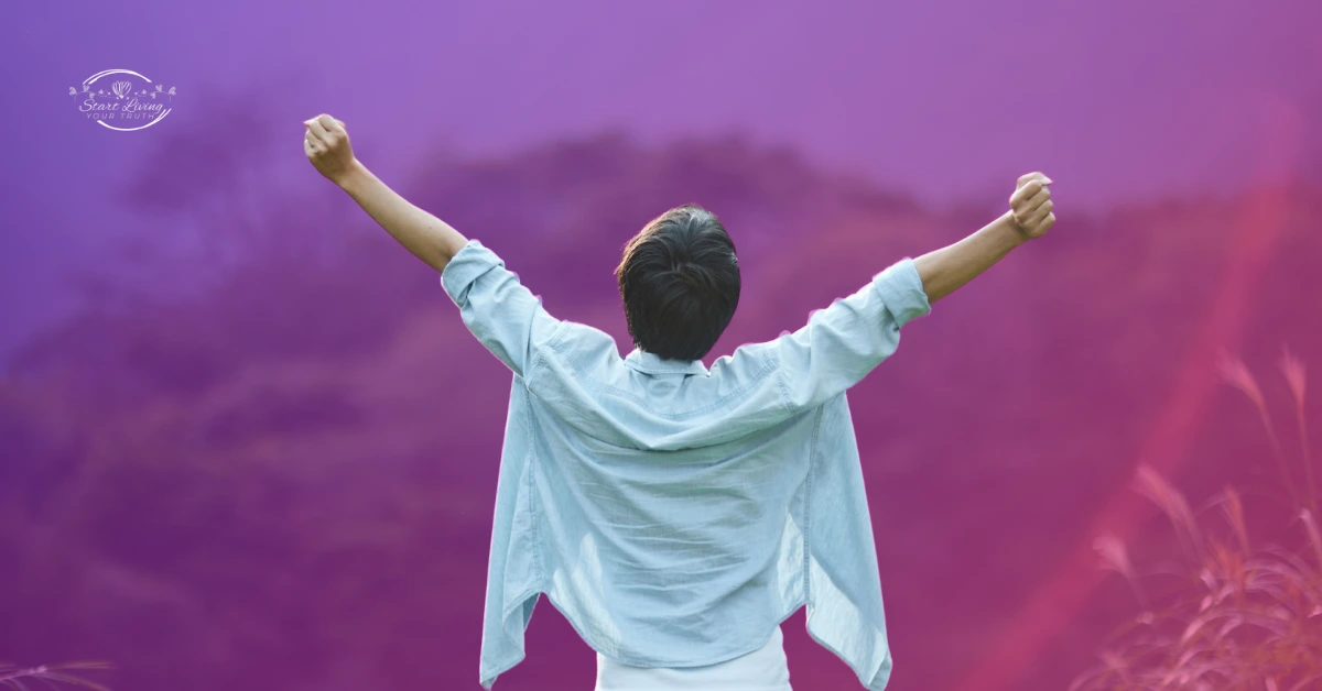 Person celebrating with arms raised outdoors, colourful background.