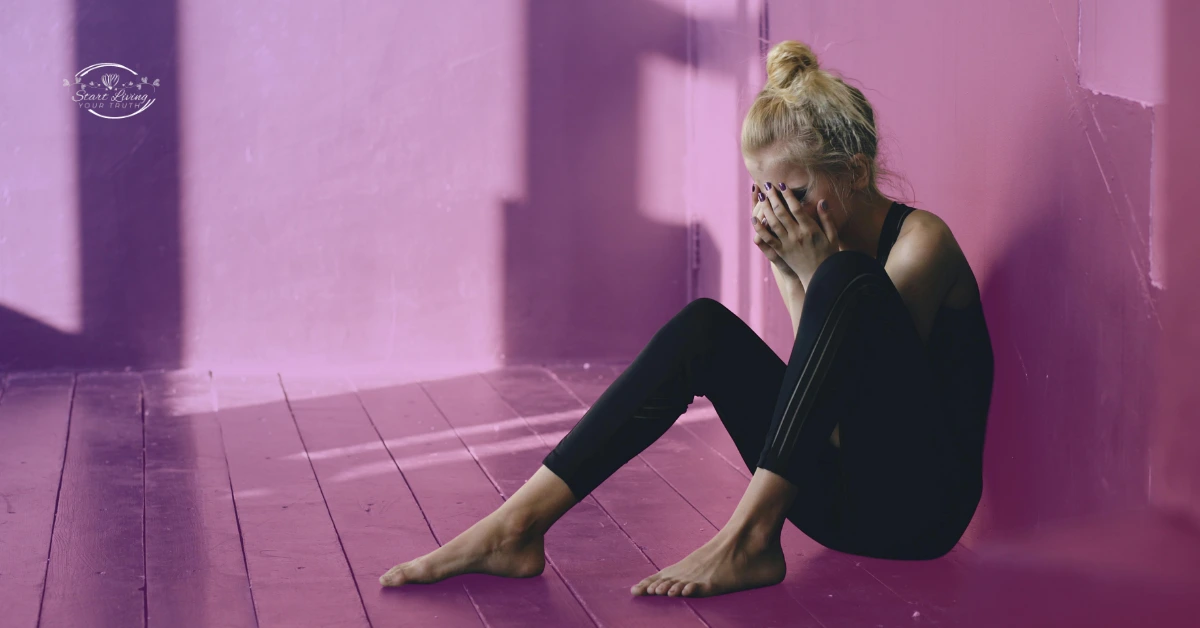 Woman sits upset in corner, covering face.