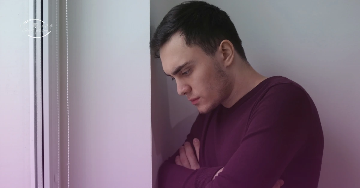 Pensive man leaning against wall indoors.