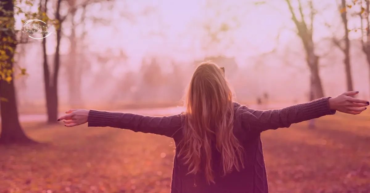 Woman embracing nature with open arms in autumn.