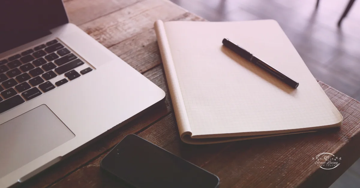 Laptop, notebook, pen, and phone on wooden desk.