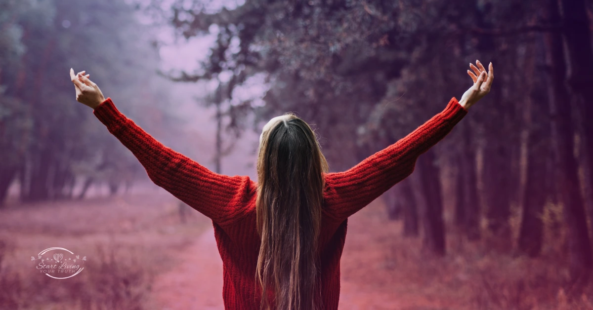 Person in red sweater with arms raised in forest