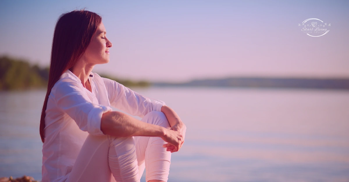 Woman meditating by a serene lake at sunset.