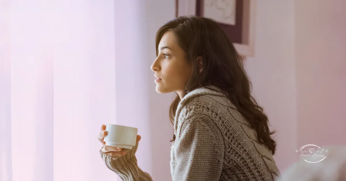 Woman in sweater holding coffee cup near window.