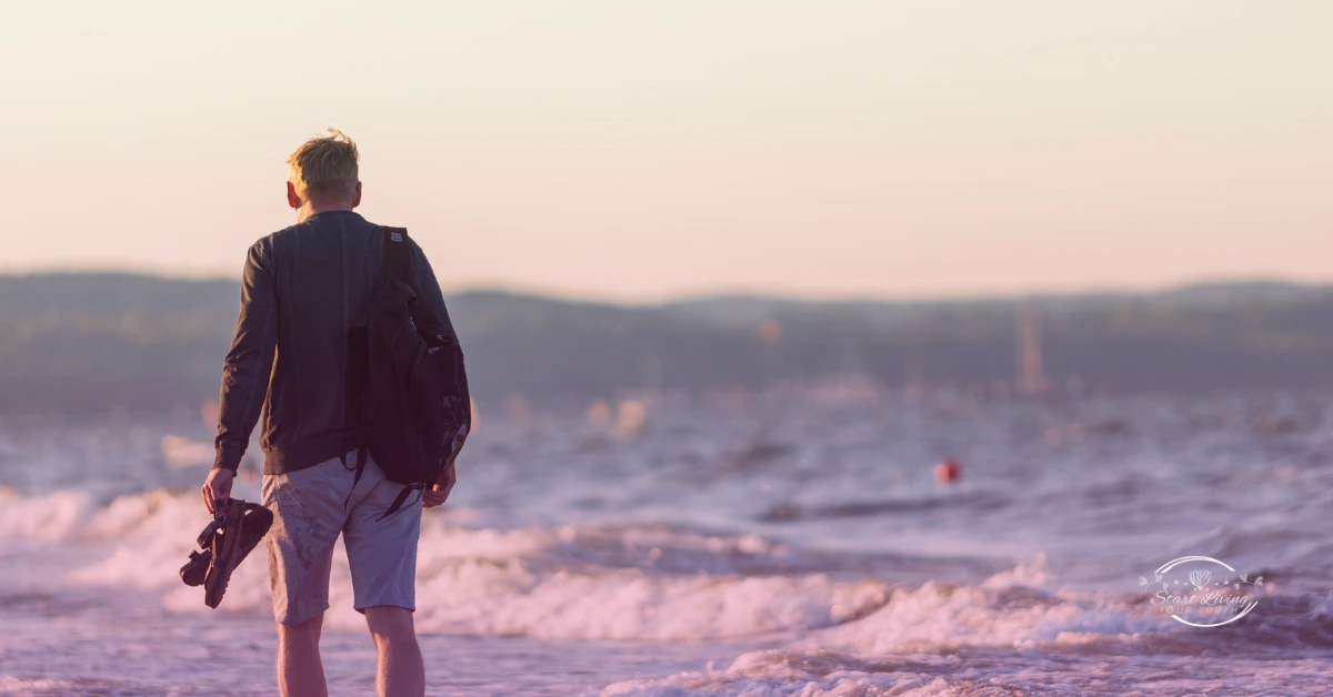 Man walking along a beach at sunset.