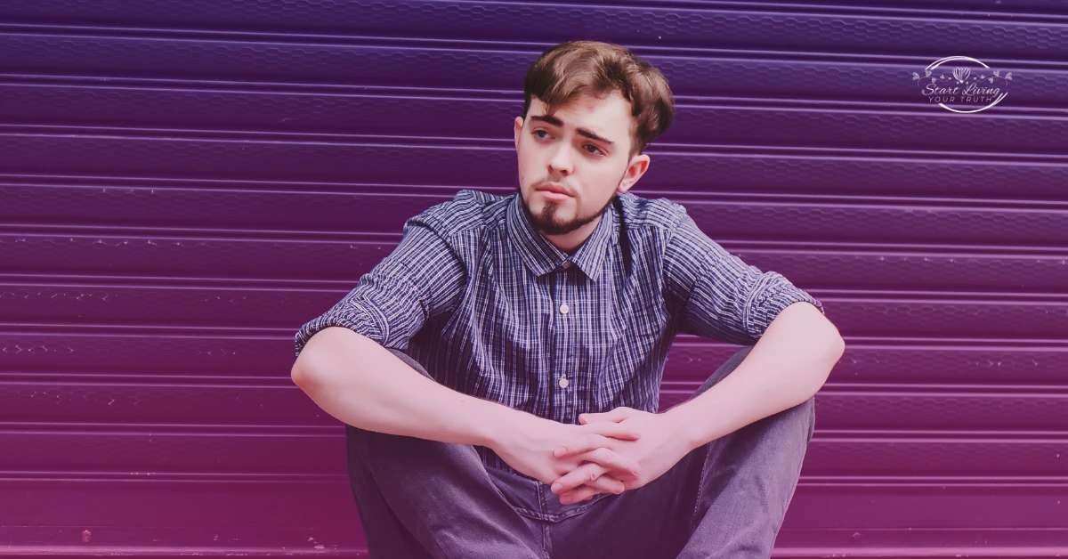 Man in plaid shirt sits against purple wall.
